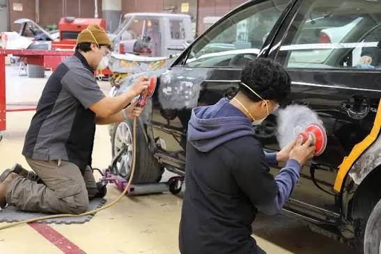 Two technicians sanding and finishing panels on a black car