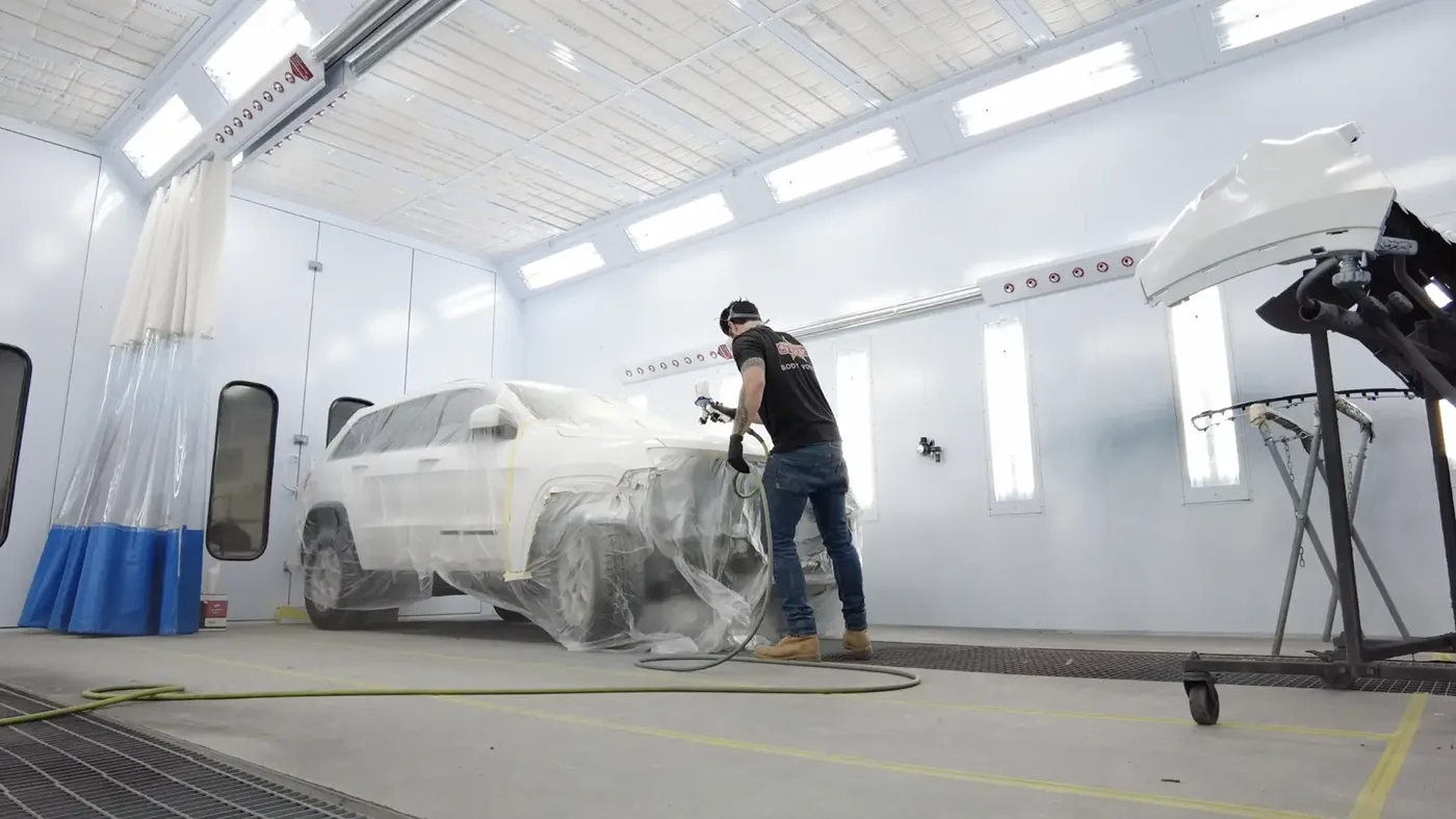 A painter refinishing a masked vehicle inside a professional spray booth