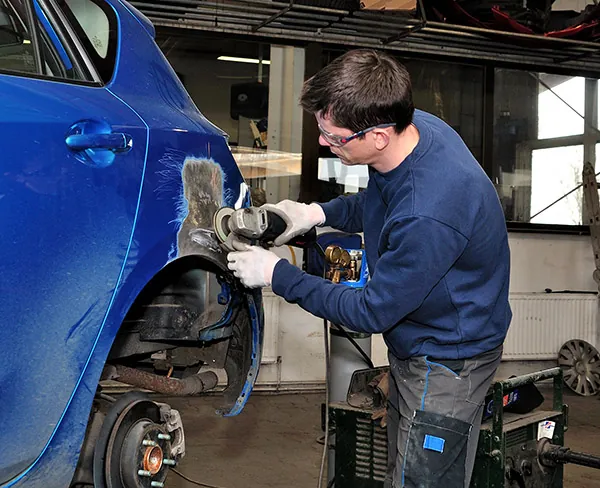 A technician grinding a damaged fender on a blue car