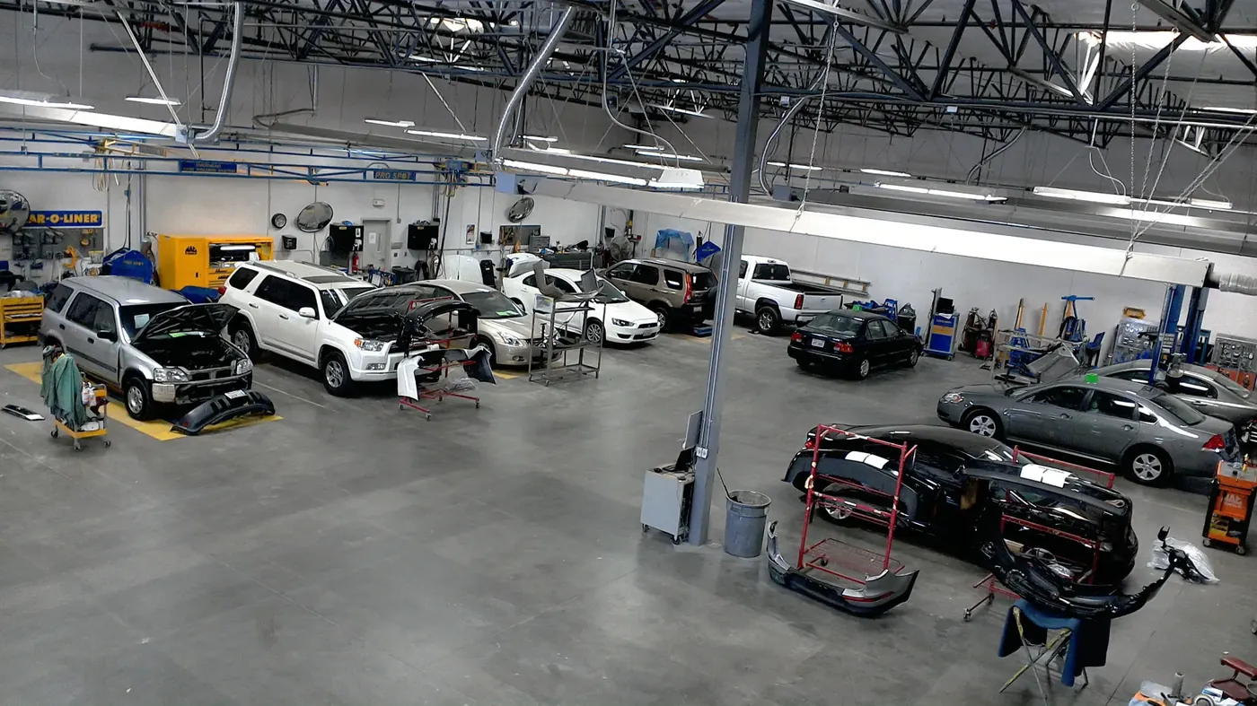 A busy collision repair shop floor with vehicles in every stage of repair