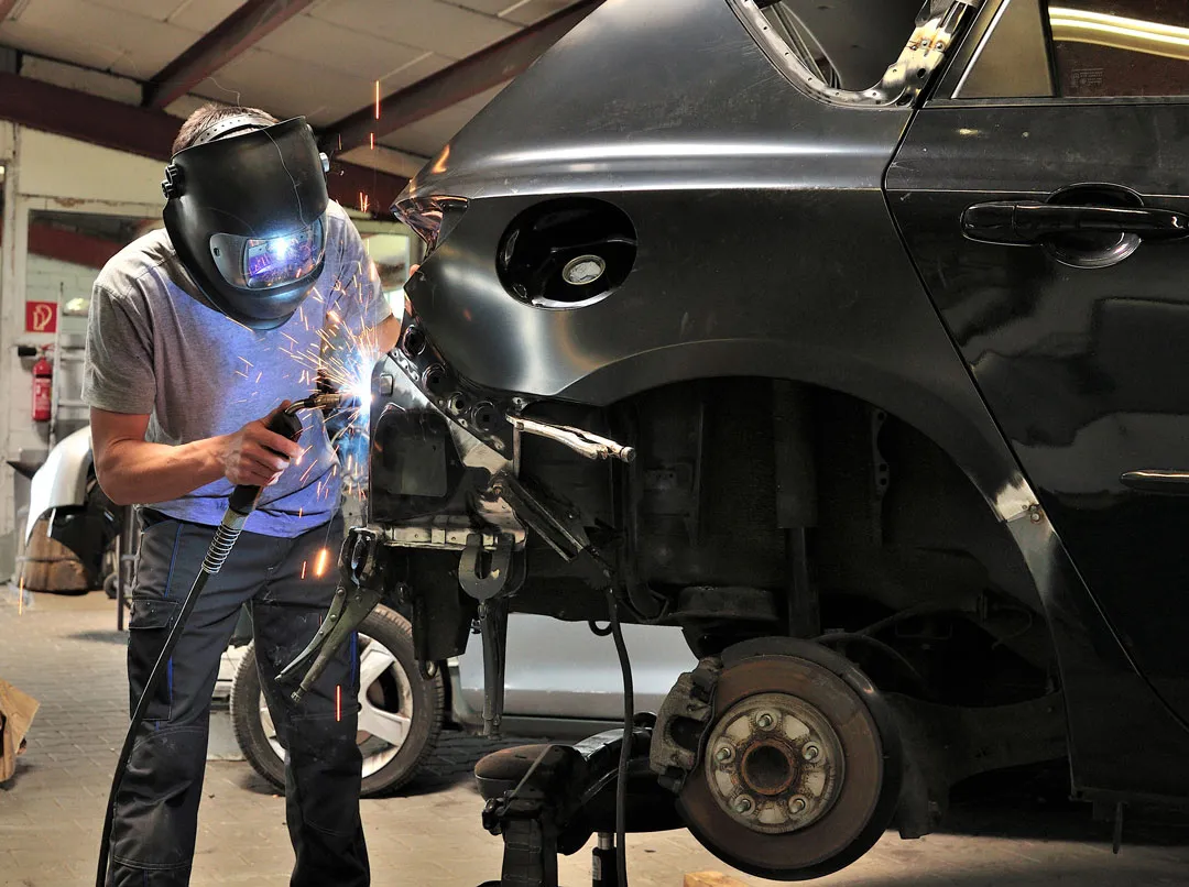 A welder repairing the rear quarter panel of a dark SUV