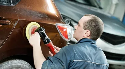 A technician machine-polishing the rear quarter of a brown car